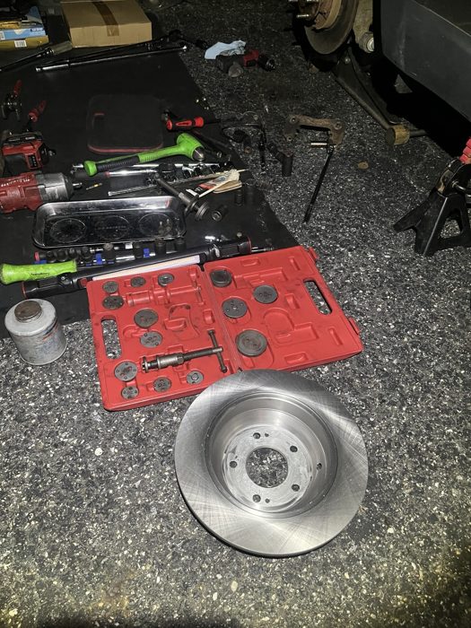 Brake rotor and mechanic tools laid out beside a vehicle